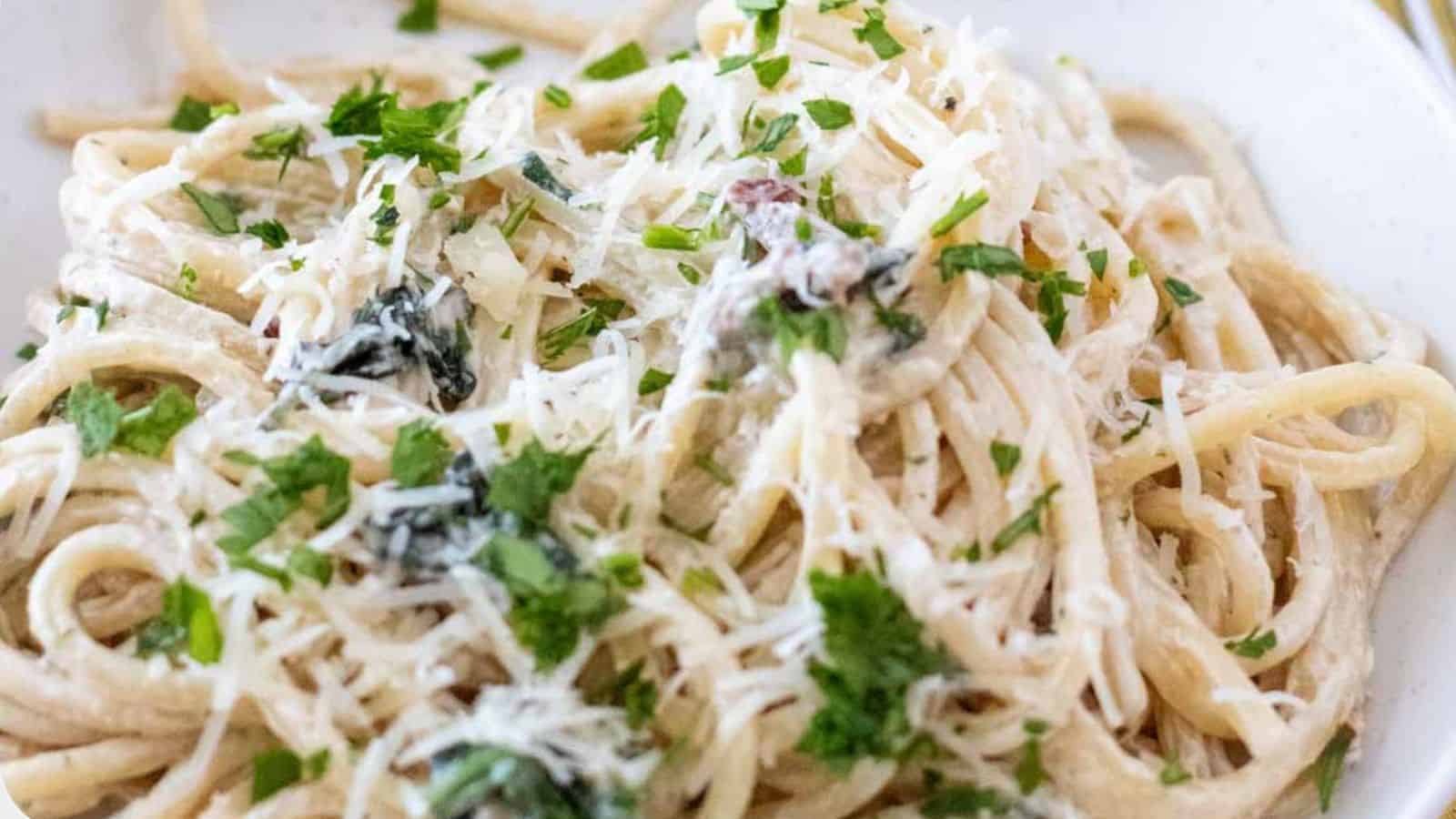 A close-up of a plate of Creamy Tuscan Pasta topped with a rich white sauce, grated cheese, and garnished with chopped parsley.