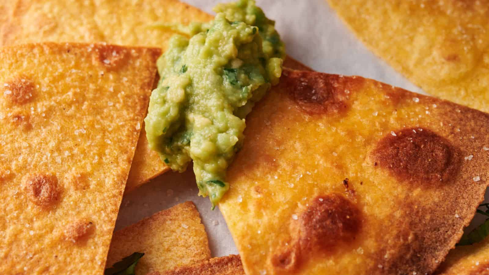 Close-up of crispy tortilla chips with a dollop of guacamole on top.