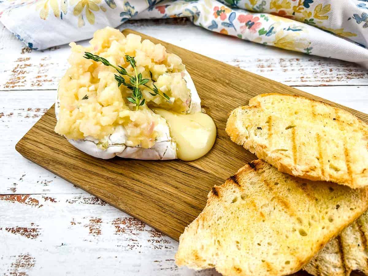 A chunk of oozing brie with apple chutney on a board.