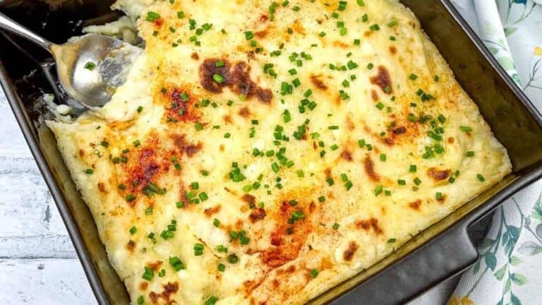 A close-up of Grandma's Mashed Potato Casserole with a serving spoon in the dish.