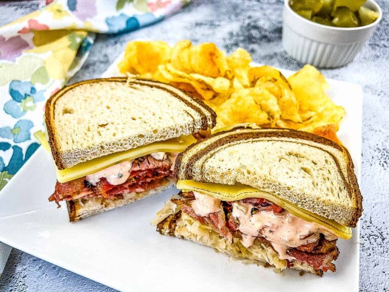 A Pastrami Reuben sandwich on a plate with chips and pickles.