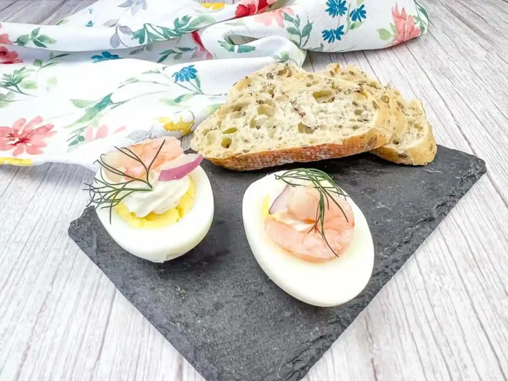 Two Pickled Shrimp Egg Shooter halves were placed on a slate board, next to slices of bread.