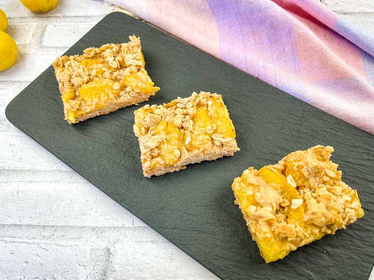 Yellow plum crumble bars on a black slate plate.