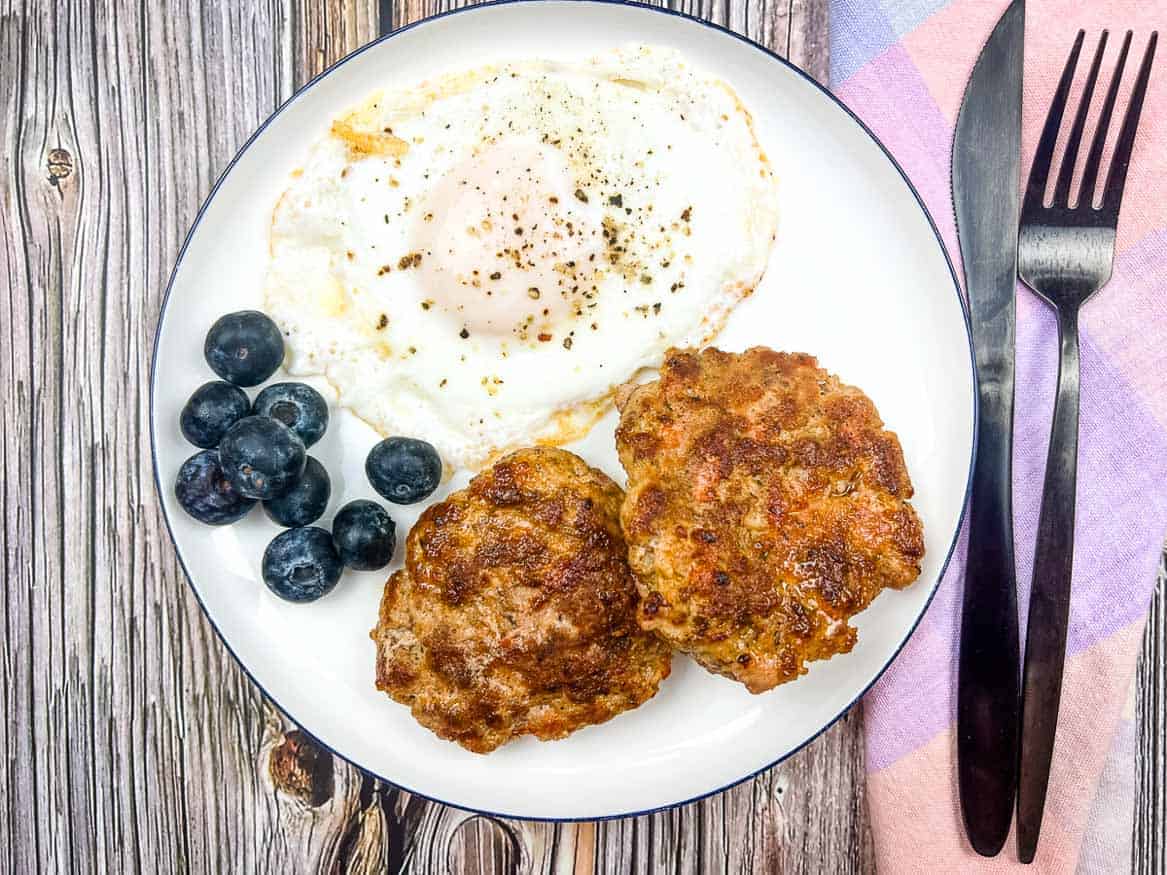 Breakfast sausage on a plate with an egg and berries.