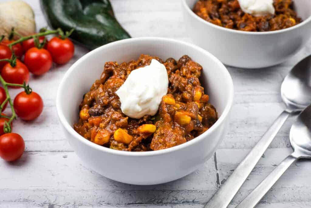 Two white bowls of Southwestern chili topped with sour cream are on a table.