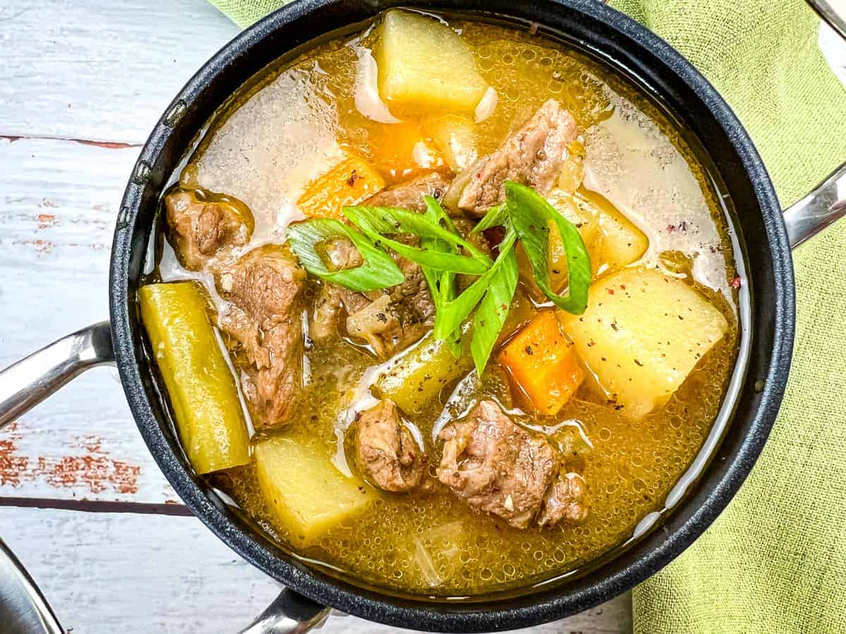 A pot of Steak and Potato Soup garnished with sliced green onions.