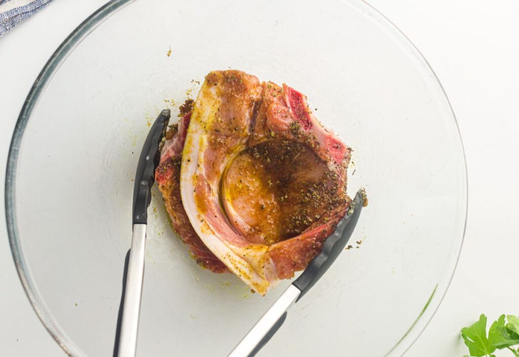 Raw pork chops coated in seasoning held with tongs.