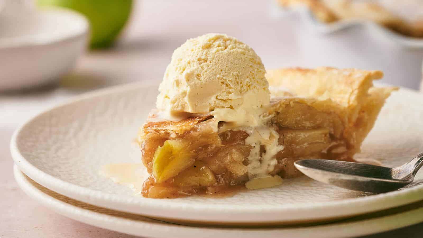 A slice of apple pie on a plate with a scoop of ice cream on top.