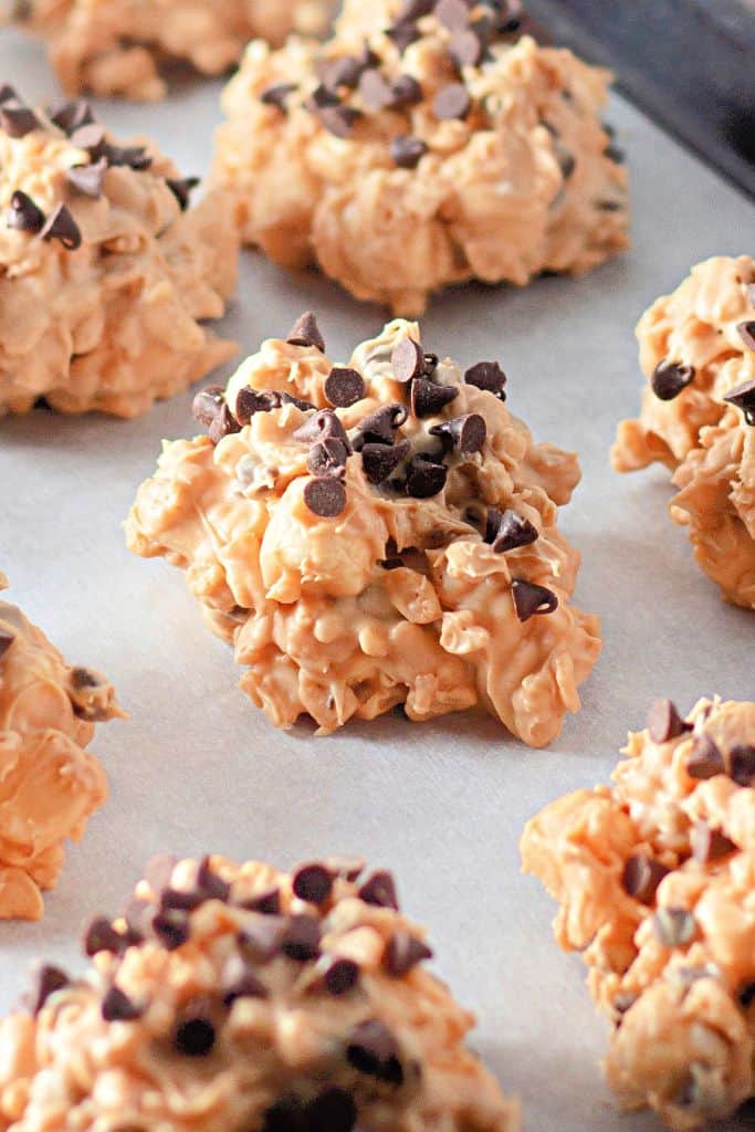 A clusters of Avalanche cookies, made with peanut butter, Rice Krispies cereal, and mini chocolate chips, arranged on a parchment-lined baking sheet.