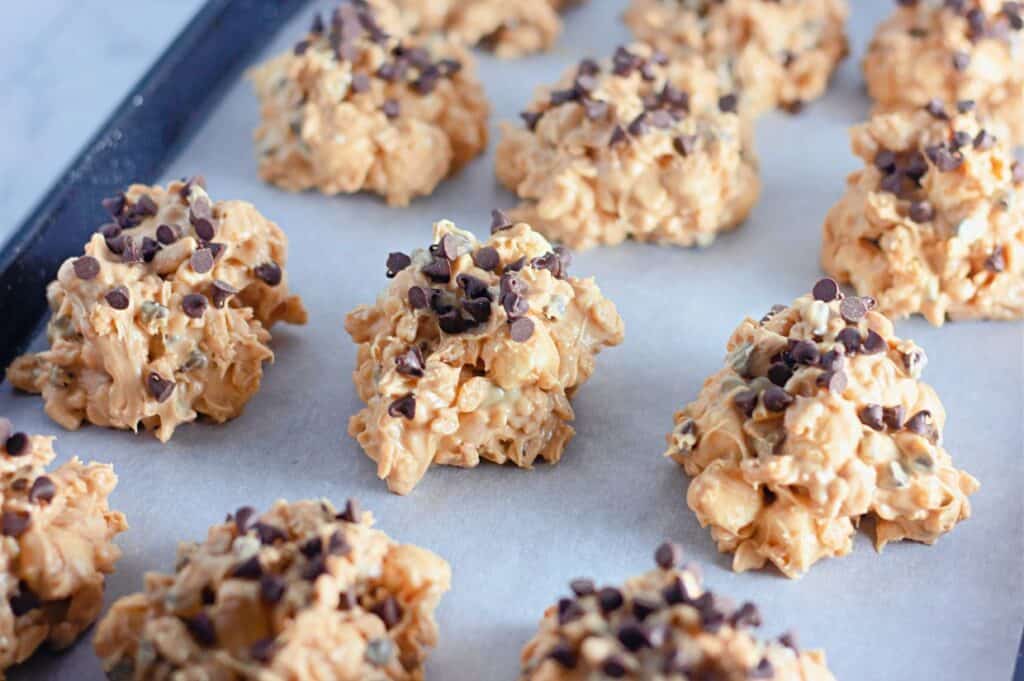 A clusters of Avalanche cookies, made with a mixture of peanut butter and chocolate chips, arranged on a baking sheet lined with parchment paper.