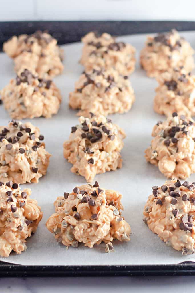 A batch of Avalanche cookies, made with peanut butter, Rice Krispies cereal, and mini chocolate chips, arranged on a parchment-lined baking sheet.