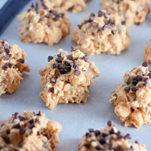 A clusters of Avalanche cookies, made with a mixture of peanut butter and chocolate chips, arranged on a baking sheet lined with parchment paper.