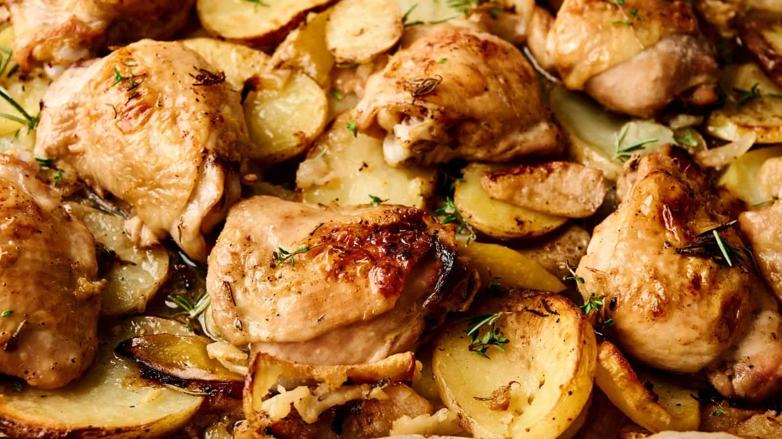 Roasted chicken thighs with sliced potatoes garnished with herbs.