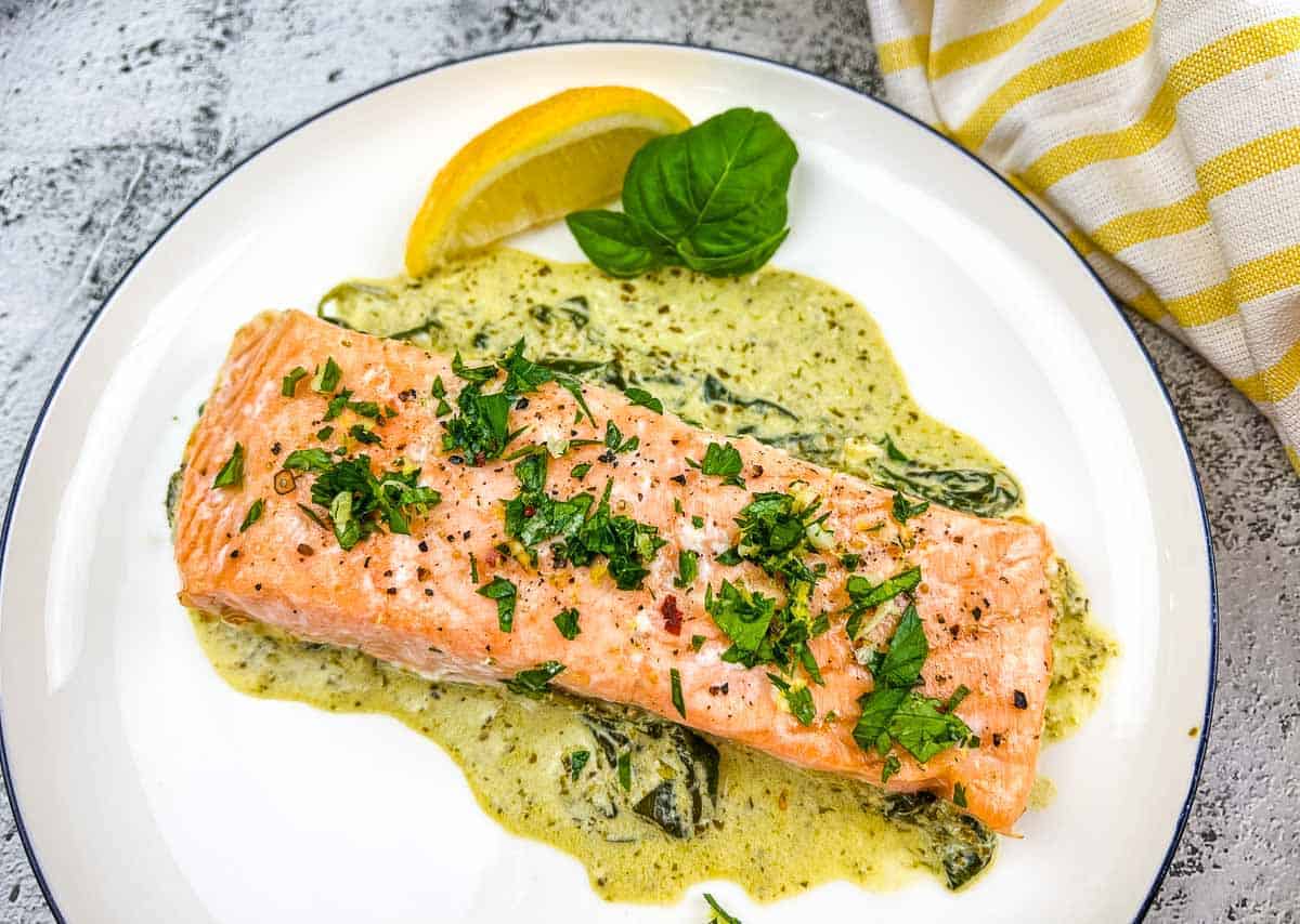 Baked Pesto Salmon with spinach sauce on a white plate.