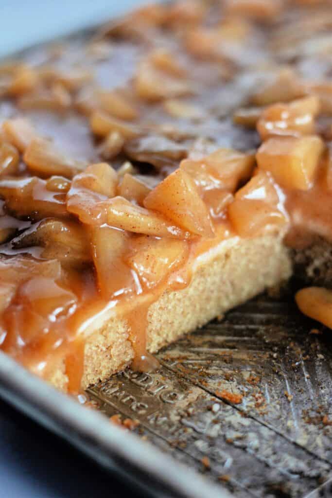 A close-up of caramel apple sheet cake with caramelized apple topping, showing a slice cut from the tray.