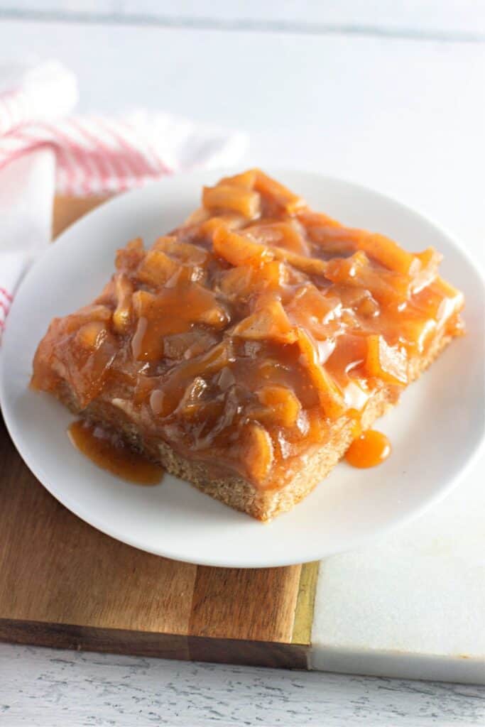 A slice of caramel apple sheet cake topped with a rich caramelized apple topping, served on a white plate.