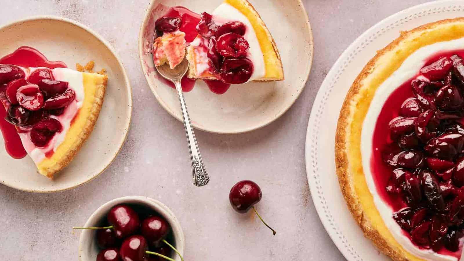 Slices of Cherry cheesecake topped with cherry sauce, served on plates with fresh cherries on the side.