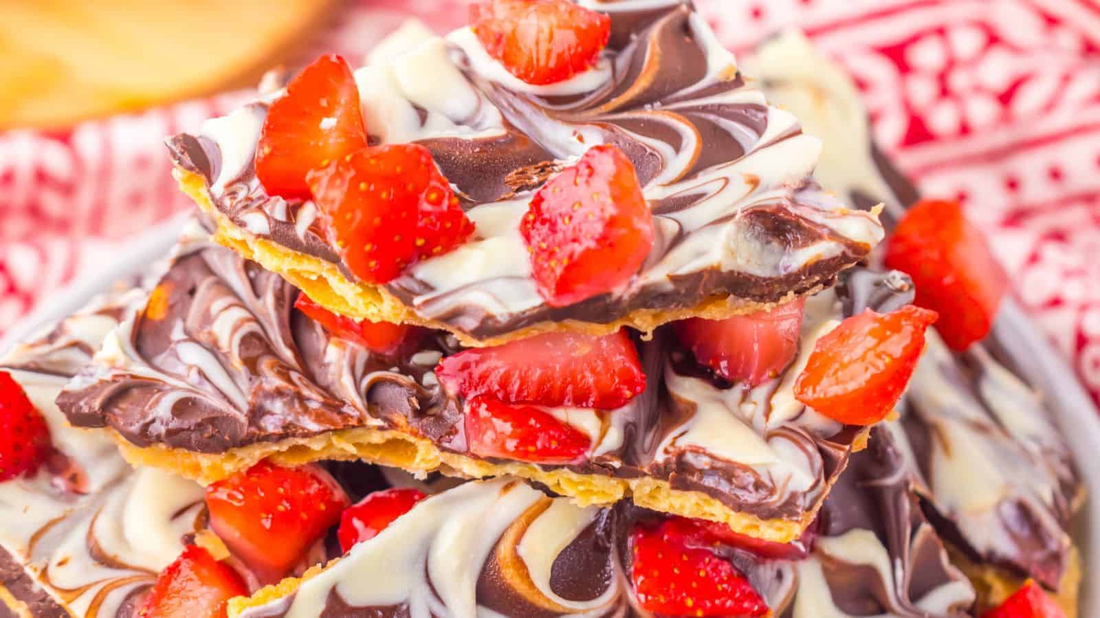 Stack of chocolate bark with swirled dark and white chocolate, topped with fresh sliced strawberries, on a red patterned cloth background.