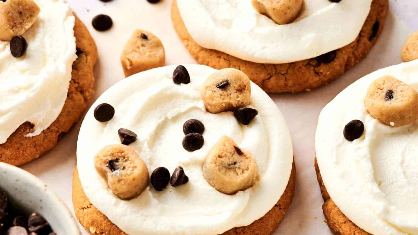 Copycat Crumbl Cookie Dough Cookie topped with white frosting, chocolate chips, and small cookie dough pieces.