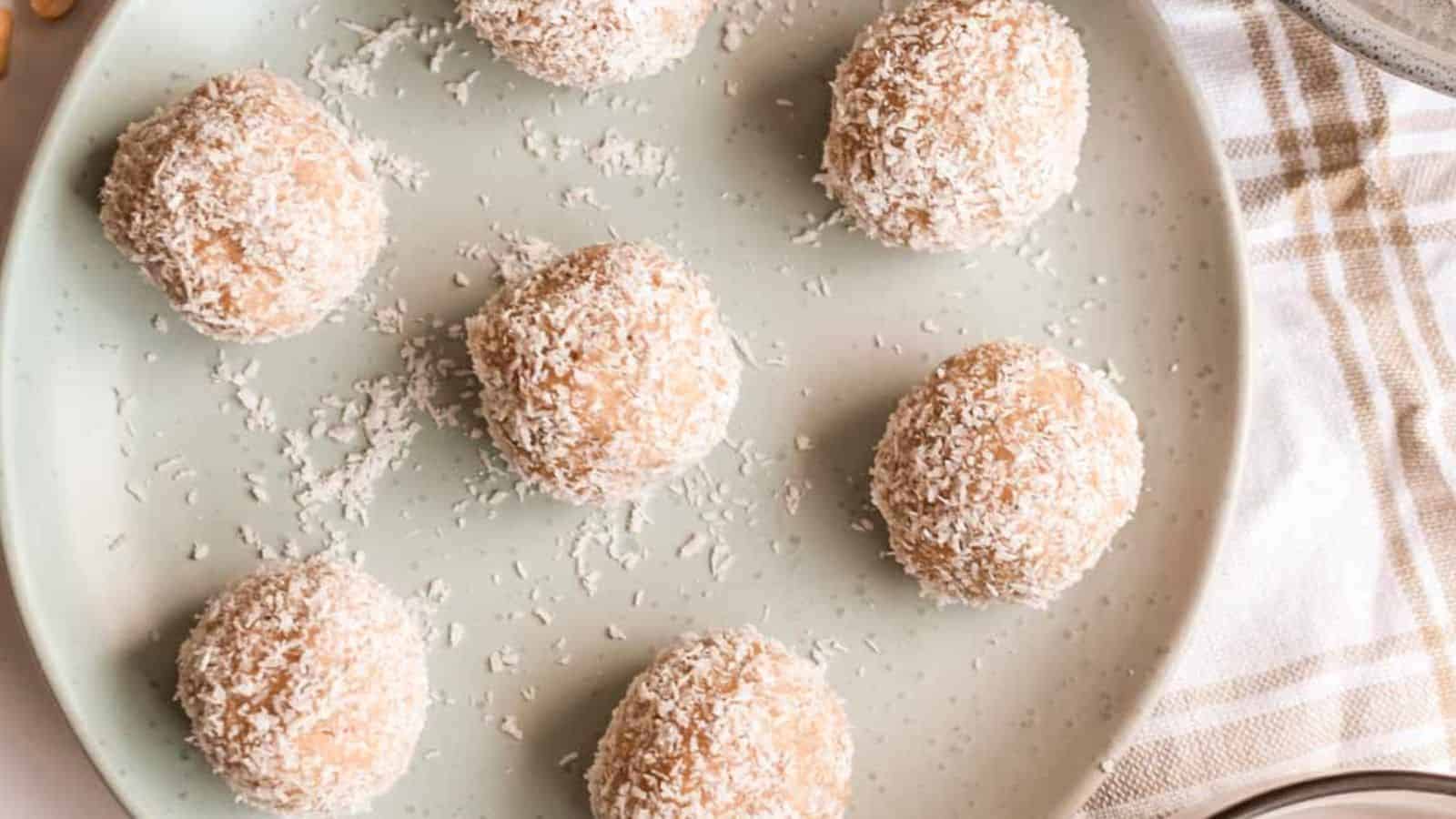 Easy peanut butter bliss balls coated in shredded coconut, arranged on a plate with a checkered cloth in the background.