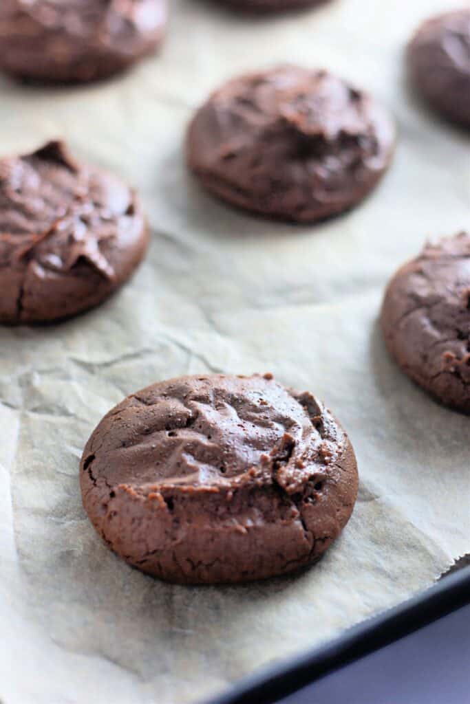 Close-up of freshly baked fudgy chocolate brownie cookies on a parchment-lined baking tray.