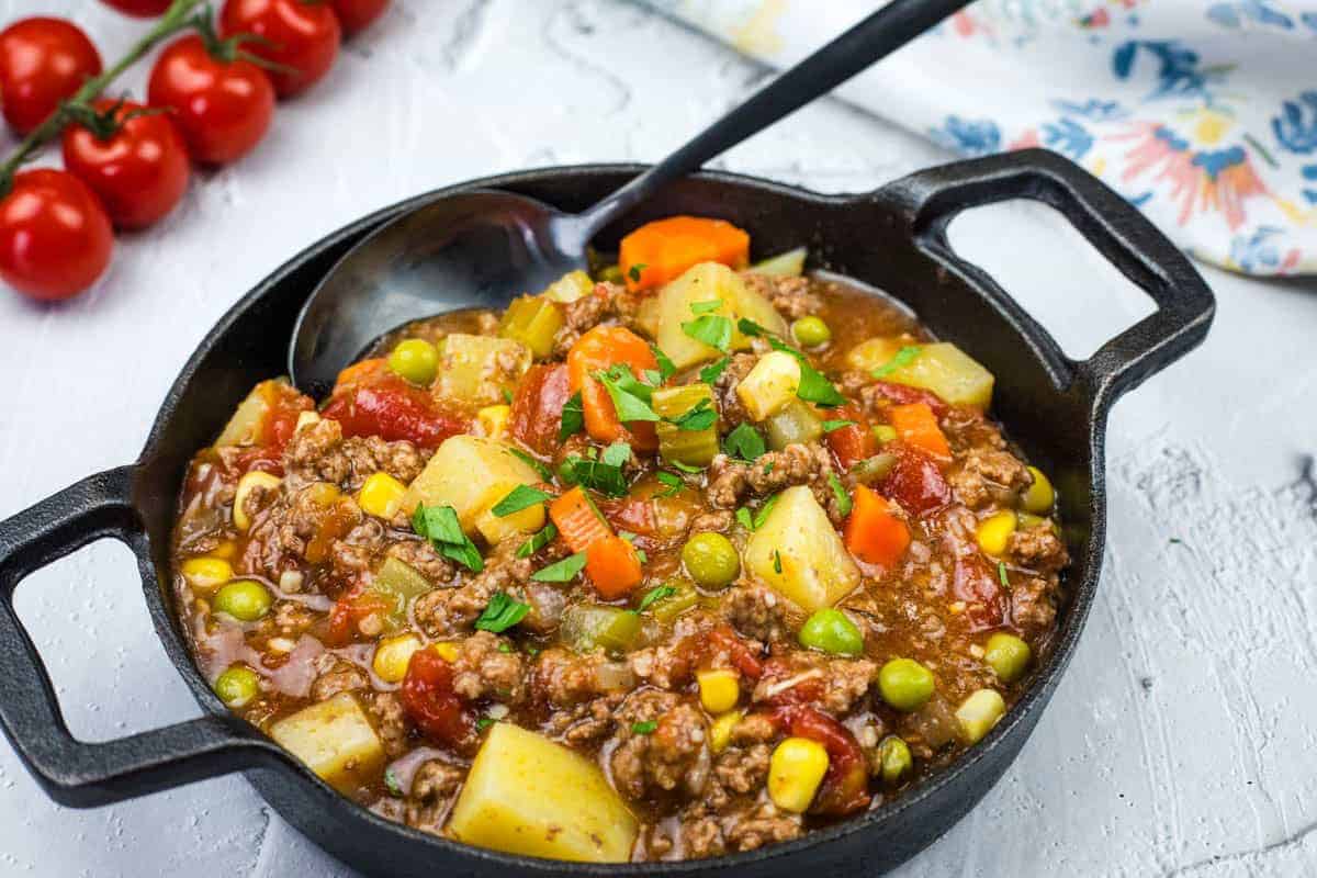 A cast iron skillet filled with Mom’s Hamburger Stew garnished with herbs.