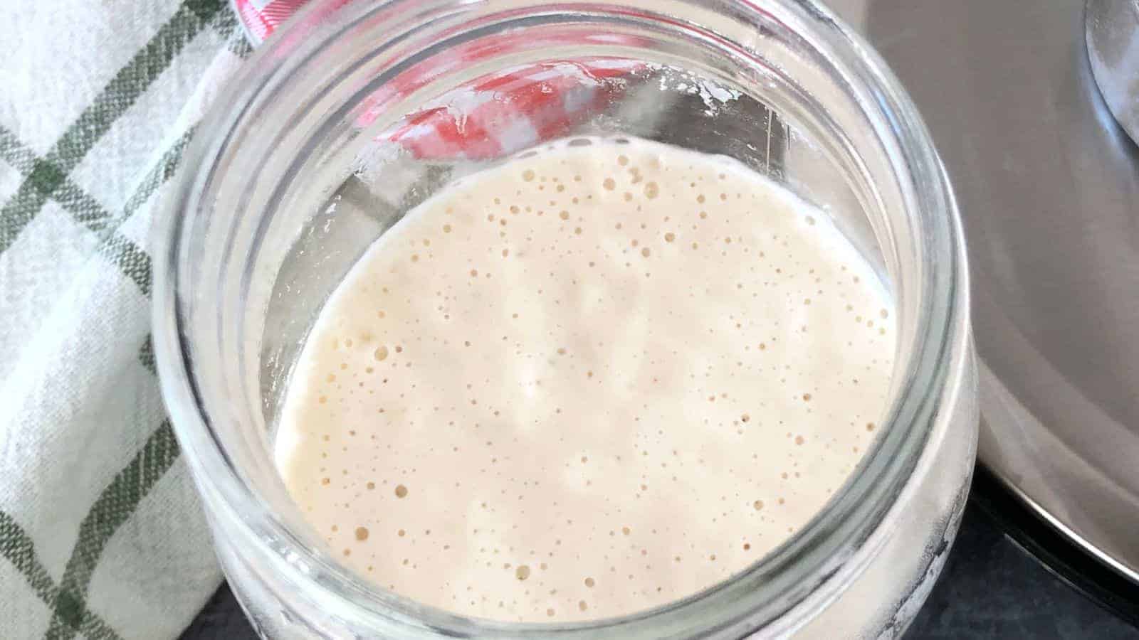 Open glass jar filled with frothy, light-beige liquid next to a green and white checkered cloth.