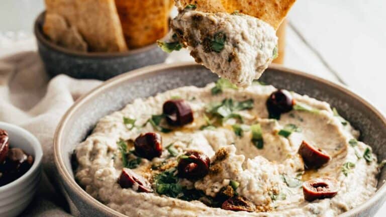 Creamy Lebanese baba ganoush garnished with olives, herbs, and spices, served with crispy pita chips.