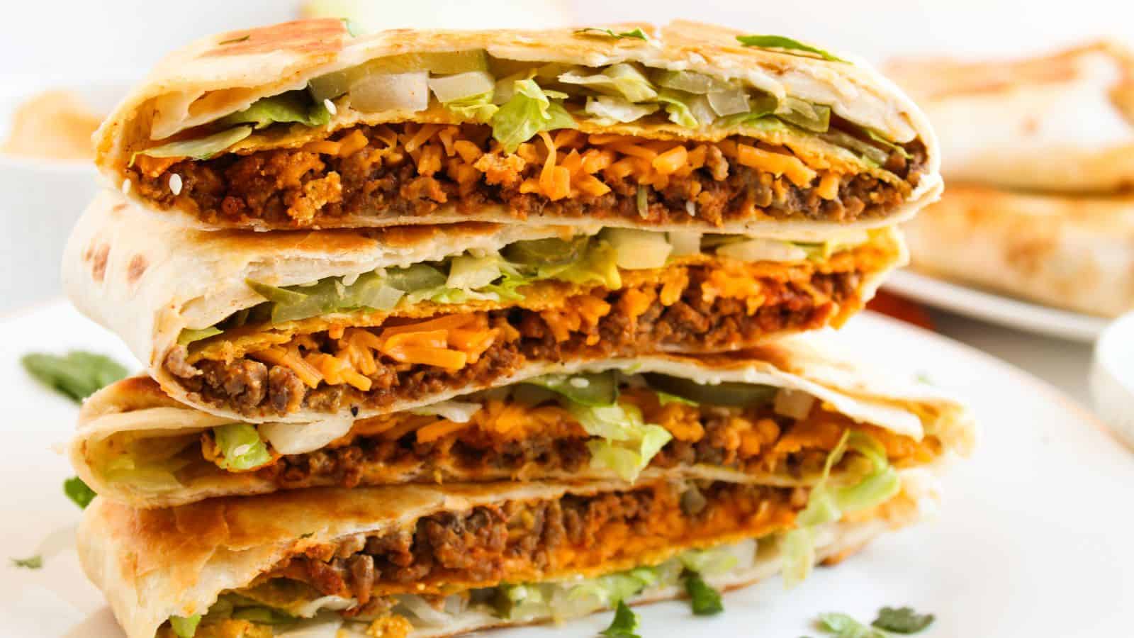 Close-up of a stack of folded tortillas filled with beef, melted cheese, lettuce, and onions on a white plate.