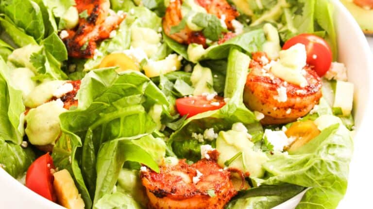 A fresh salad with grilled shrimp, cherry tomatoes, avocado, feta cheese, and lettuce.
