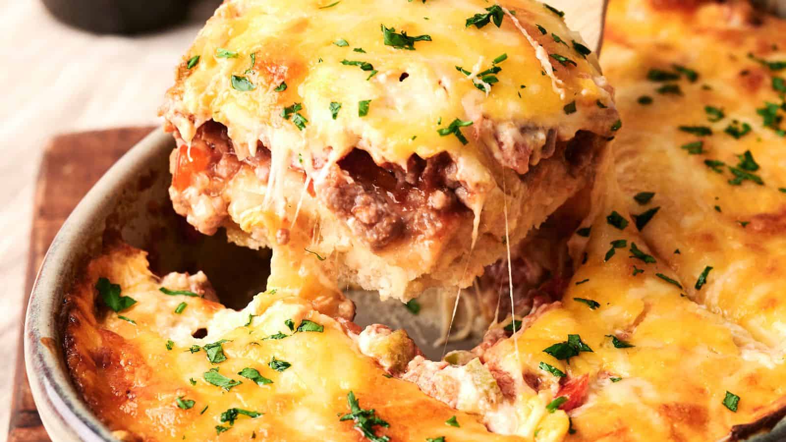 A slice of cheesy lasagna being lifted from a baking dish, topped with melted cheese and parsley.