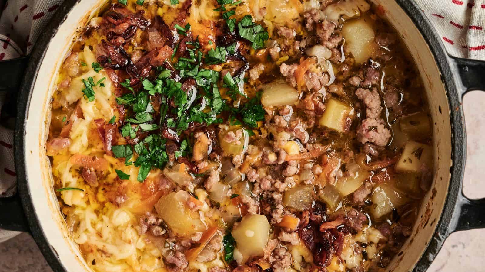 A pot of cheesy potato and meat stew garnished with chopped parsley and crispy bacon.