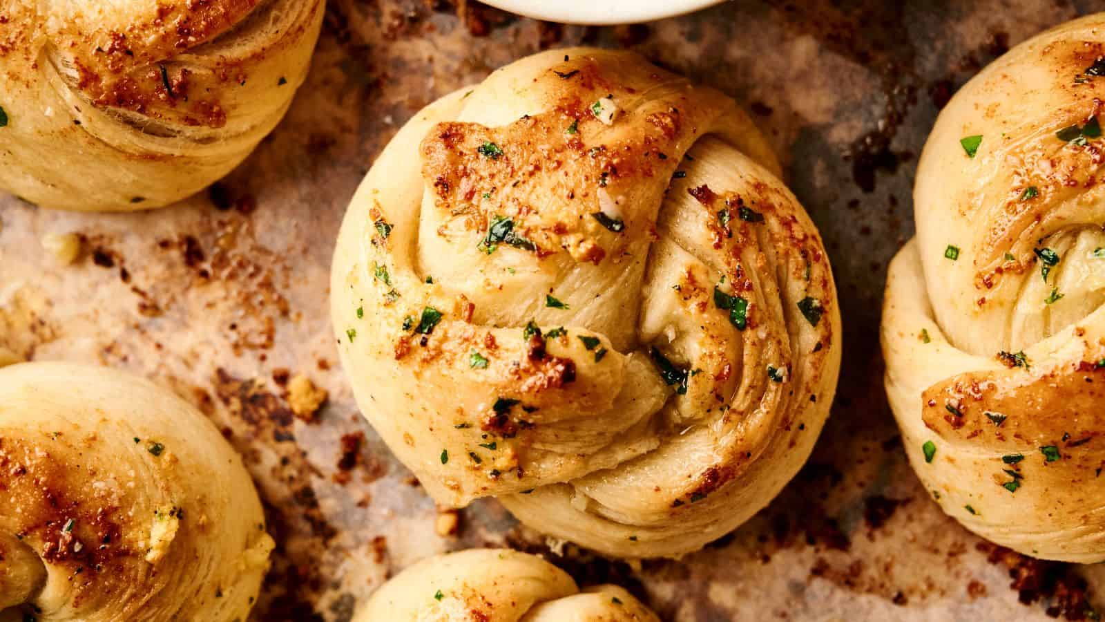 Close-up view of freshly baked garlic knots with parsley and seasoning, resting on a parchment-lined baking tray.