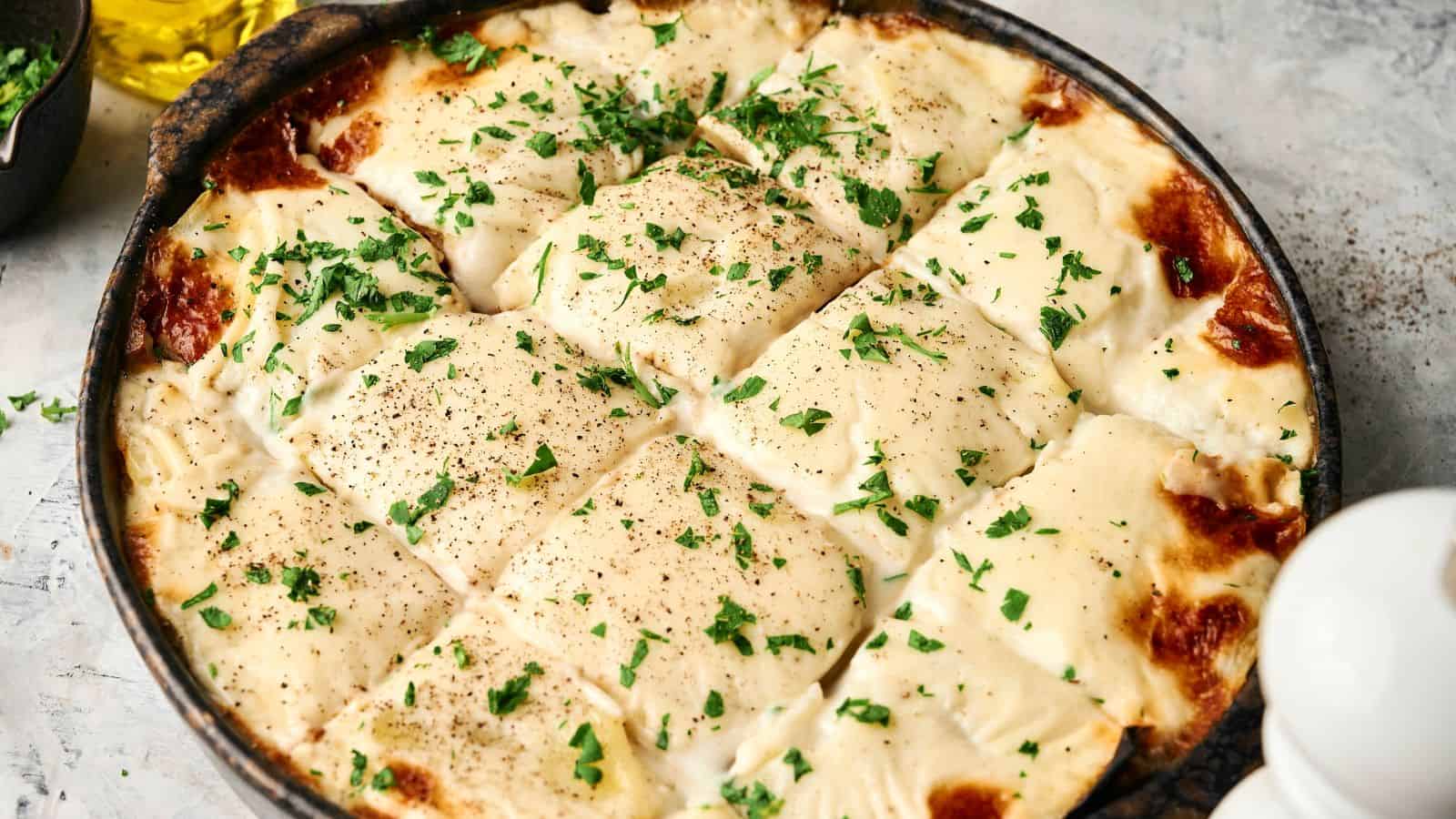 A pan of cooked lasagna topped with melted cheese, black pepper, and chopped parsley.