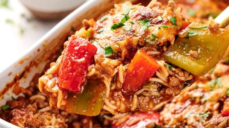 A close-up of a spoonful of casserole containing rice, ground meat, red and green bell peppers, and melted cheese.