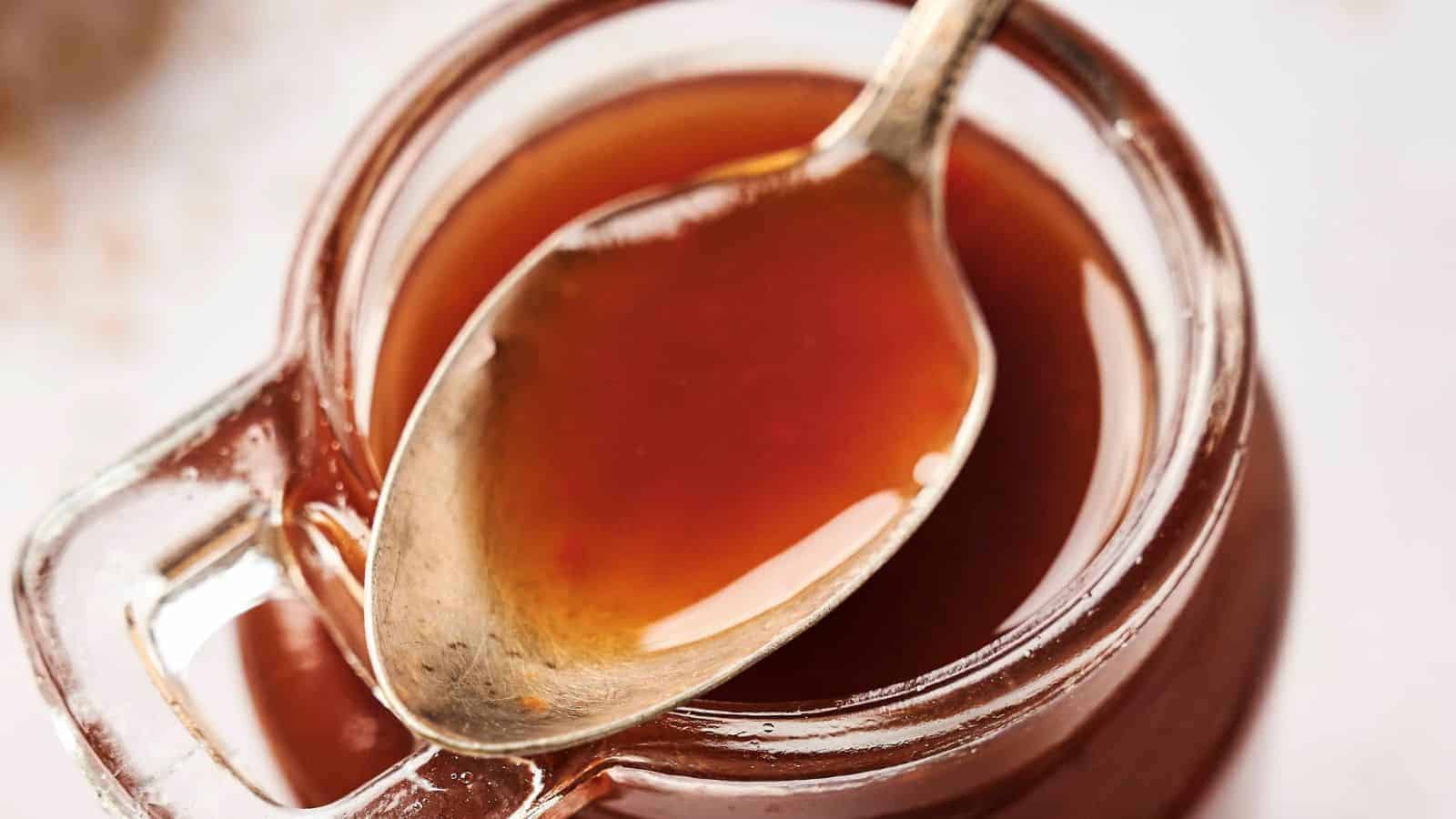 A spoon rests inside a glass jar filled with a thick, brown liquid.