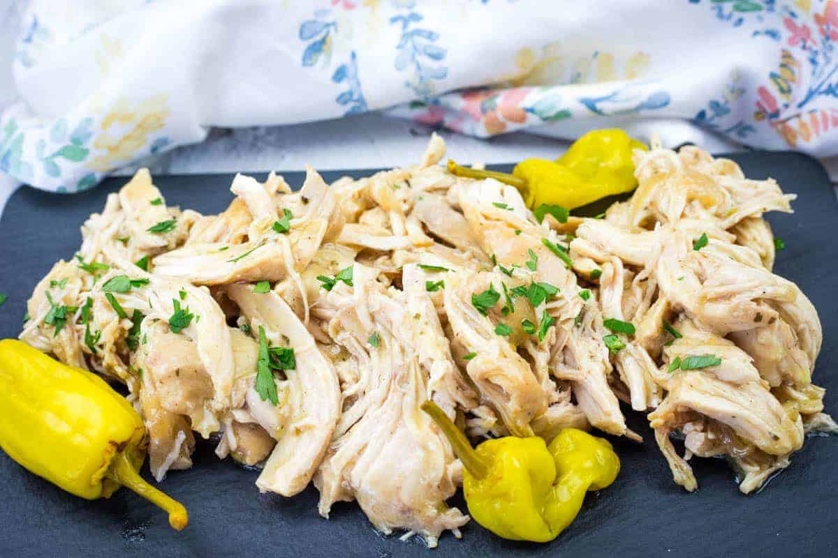 Low-Carb Mississippi Chicken garnished with parsley is served on a slate platter with yellow peppers.