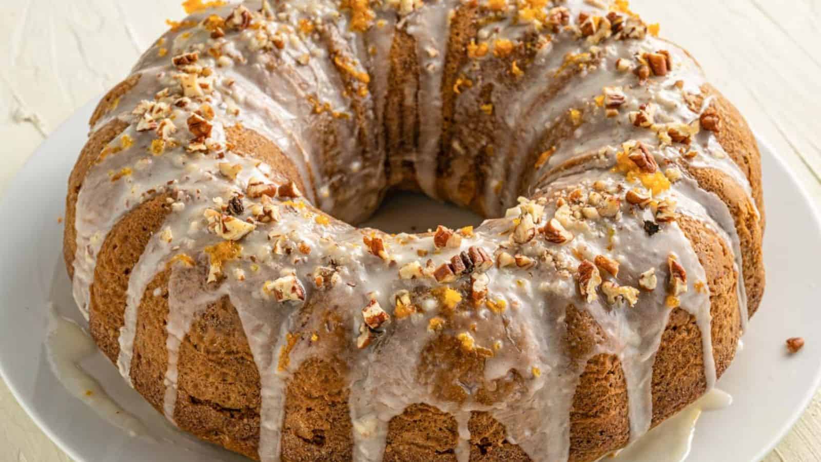 Orange & Pecan Bundt Cake drizzled with glaze and topped with chopped pecans on a white plate.