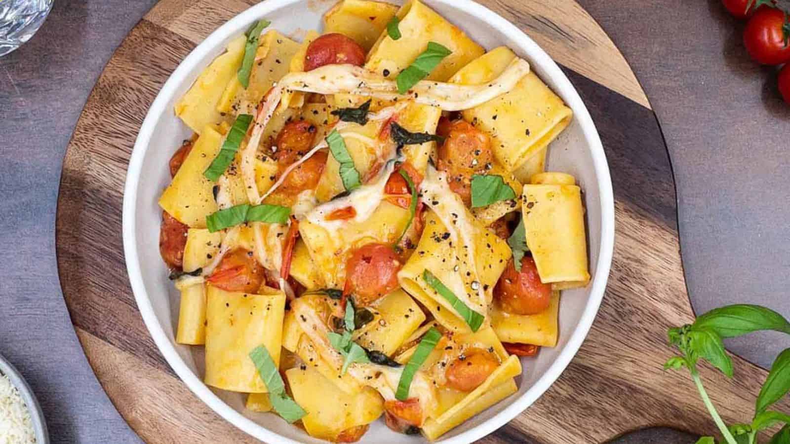 Pasta in a bowl with cheese, tomatoes, and fresh basil.