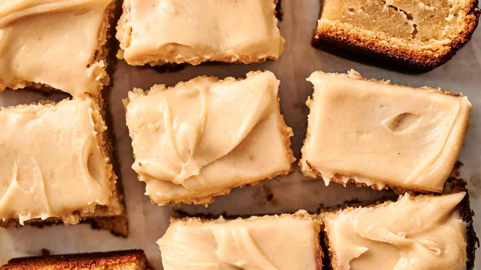 Close-up of frosted square cake pieces with a light brown crust on parchment paper.