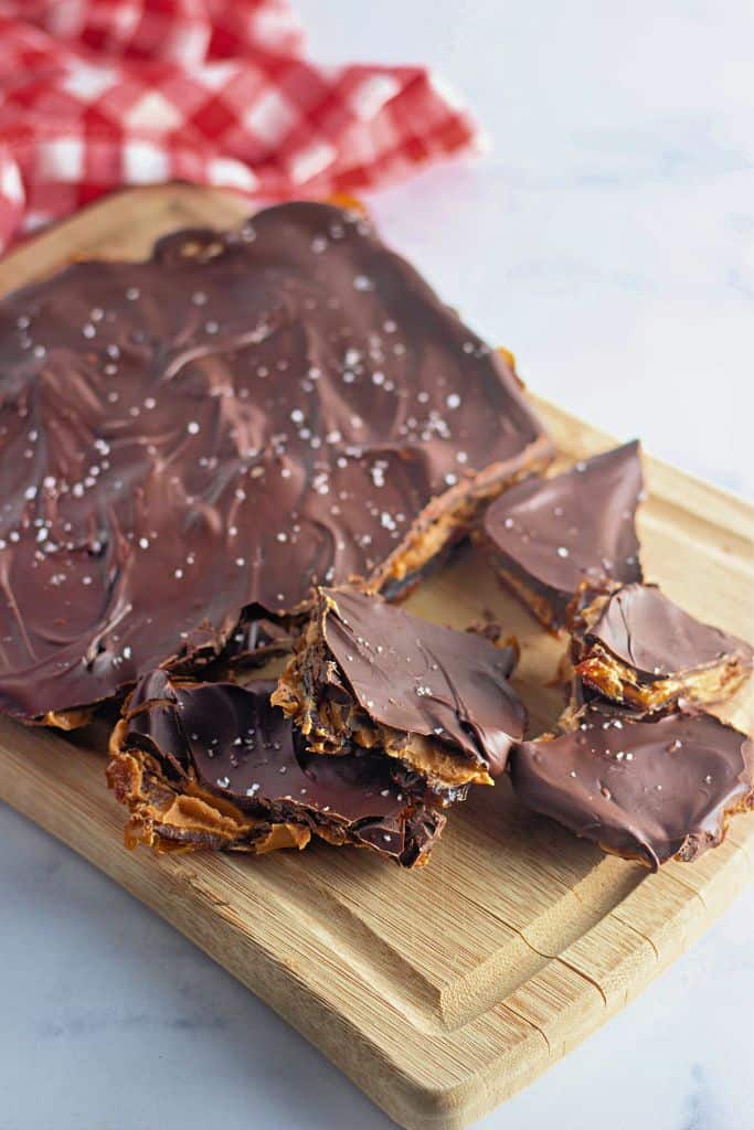 A broken pieces of chocolate bark topped with dark chocolate and sea salt, placed on a wooden cutting board.