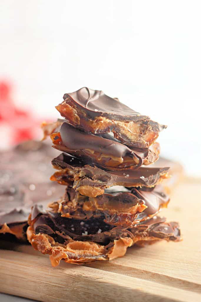 A stack of broken pieces of chocolate bark with dark chocolate and sea salt, placed on a wooden cutting board.