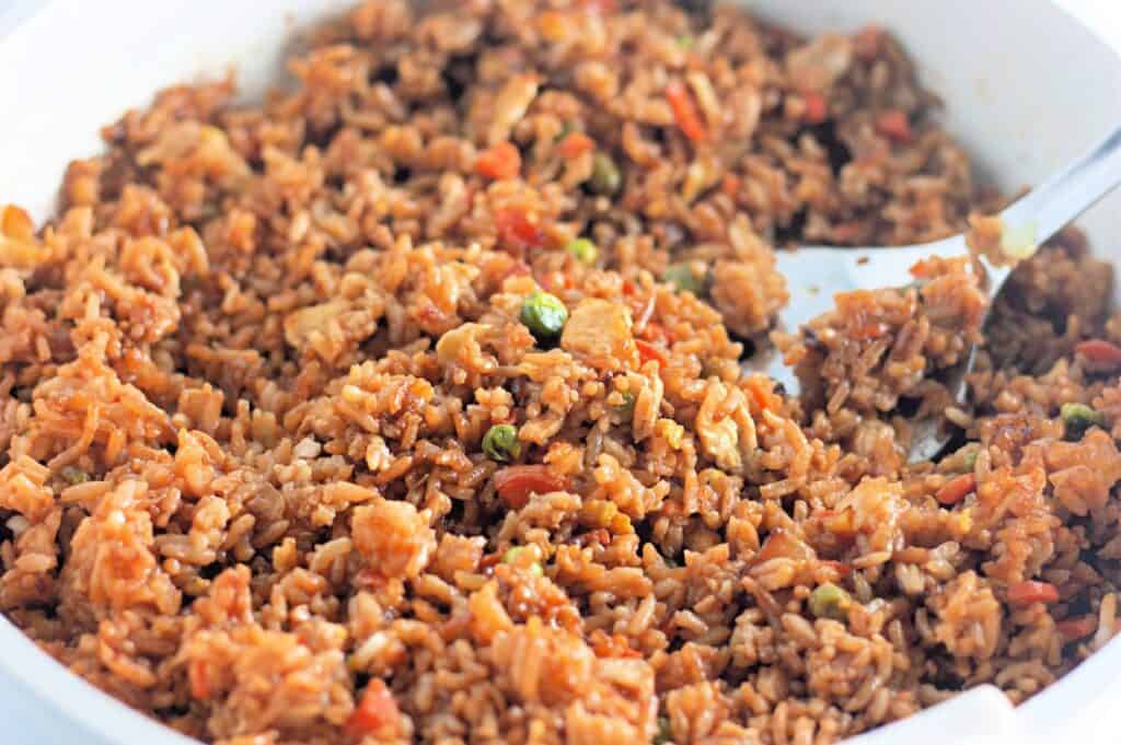 A close-up of a pan filled with homemade fried rice, featuring fluffy rice mixed with diced vegetables, small pieces of meat, and soy sauce.