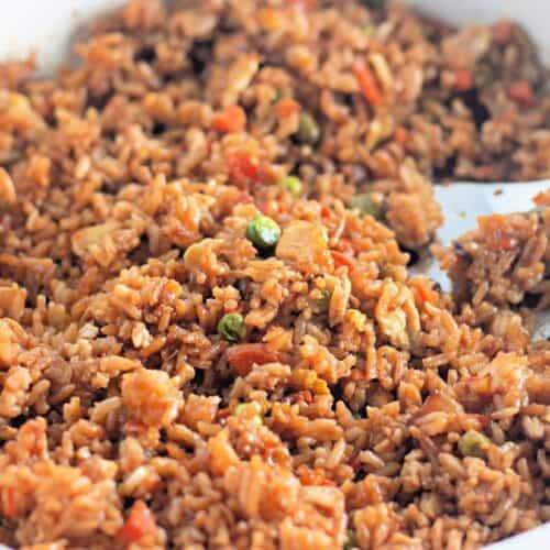 A close-up of a pan filled with homemade fried rice, featuring fluffy rice mixed with diced vegetables, small pieces of meat, and soy sauce.