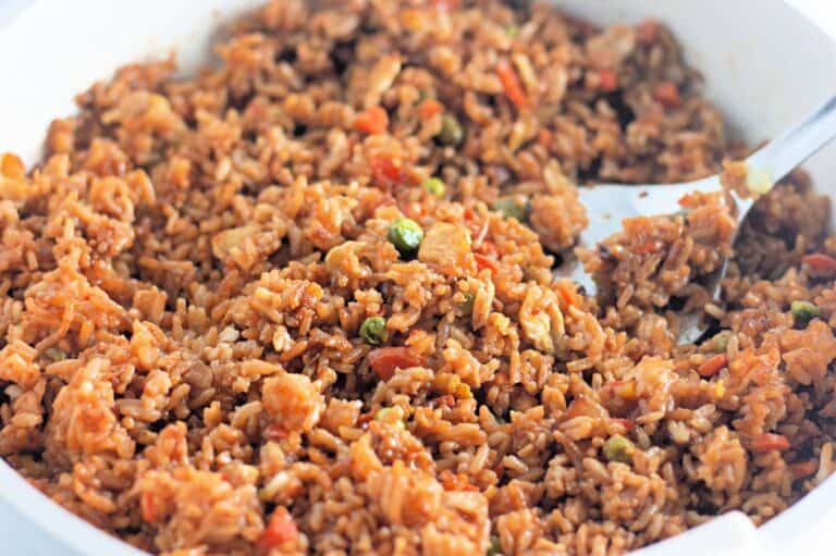 A close-up of a pan filled with homemade fried rice, featuring fluffy rice mixed with diced vegetables, small pieces of meat, and soy sauce.