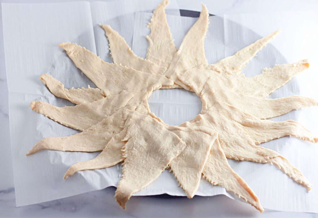 Crescent roll dough triangles arranged in a circular ring on parchment paper, with points facing outward and overlapping in the center.