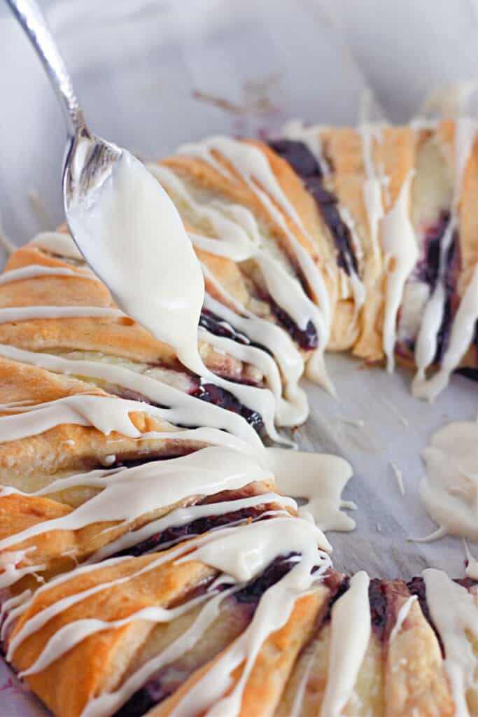 Drizzling cream cheese icing over a freshly baked raspberry crescent ring.