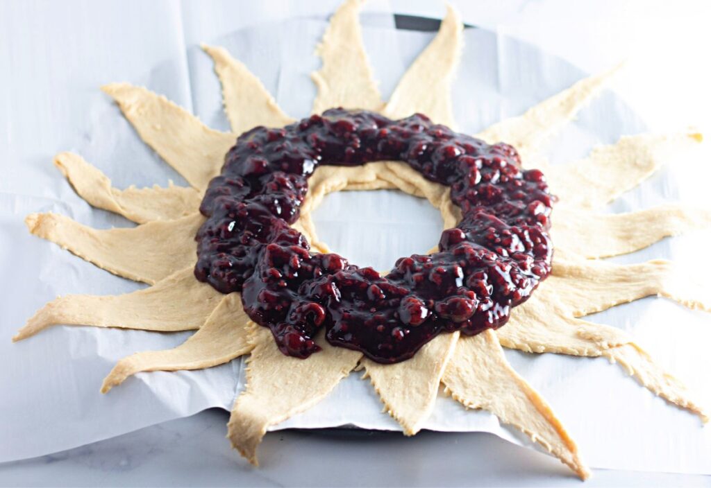 Raspberry pie filling spooned in a thick ring over the center of the arranged crescent dough.