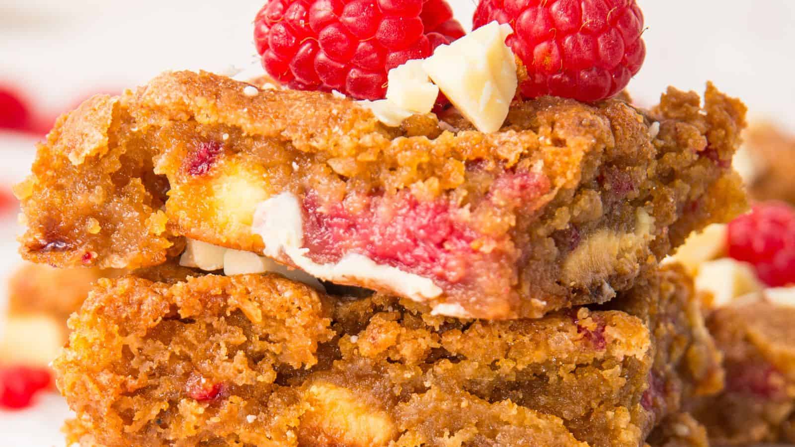 Close-up of Raspberry and White Chocolate Blondies filled with white chocolate chips and raspberries, topped with fresh raspberries and white chocolate chunks.