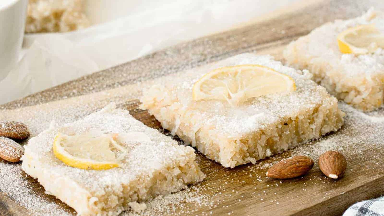 Raw lemon slice bars dusted with powdered sugar and topped with lemon slices on a wooden board.